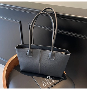Detail of black lychee-grain leather tote bag with fine stitching on a vintage chair
