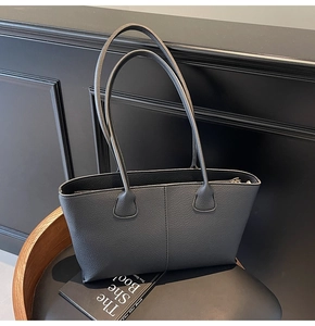 Macro detail of black lychee grain leather tote bag with vertical stitching on chair