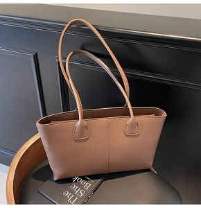 Close-up of brown litchi pattern leather tote bag with long handles on black background
