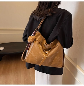 Side view of large brown crossbody bag with bear pendant and scarf detail