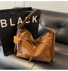 Detail of vintage brown large crossbody bag with plush bear charm on a leather sofa