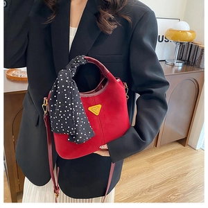 Détail macro du sac seau rouge mat avec foulard à pois et plaque logo métallique