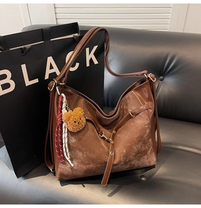 Detailed close-up of brown textured hobo bag with teddy charm on leather sofa