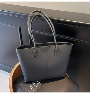 Detail of black pebbled leather tote bag with cylindrical straps and vertical stitching