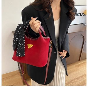 Détail du sac seau en daim rouge avec logo doré et foulard à pois sur la poignée