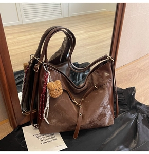 Detail of a large dark brown hobo bag with teddy bear charm and soft leather texture