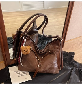 Detail of vintage brown leather tote bag with cute bear charm and striped ribbon accent