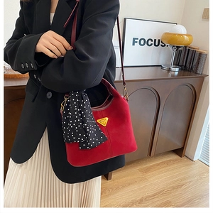 Détail du sac seau en daim rouge avec foulard à pois et logo métallique doré