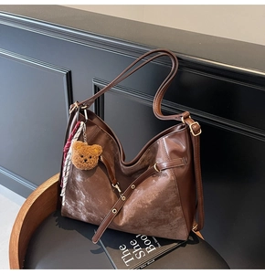 Detail of dark brown tote bag featuring mixed textures, metal ring and plush bear charm