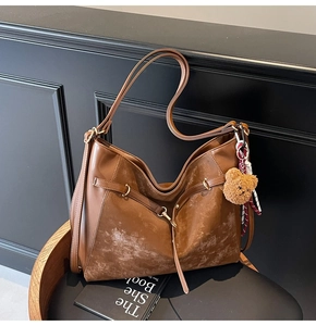 Close-up of brown textured tote bag featuring a cute plush bear charm on a dark chair