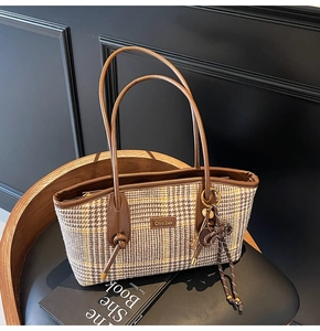 Detail der Vintage-Hahnentritt-Tasche mit braunem Lederbesatz auf einem schwarzen Stuhl