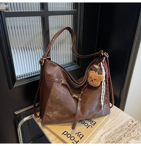 Detailed view of deep brown faux leather tote bag with teddy bear charm on books