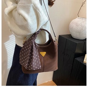 Détail du sac seau marron foncé avec anse en soie et logo triangulaire métallique