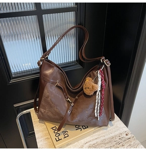 Detail view of large vintage brown hobo bag with teddy bear charm on decorative props