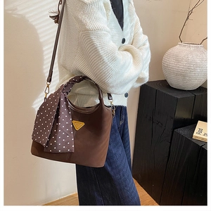 Détail d'un sac seau marron avec poignée tressée et foulard en soie porté par un modèle