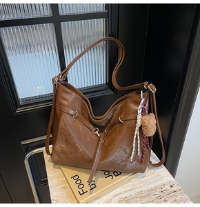 Detail of a large brown leather hobo bag with a cute bear charm and metal hardware