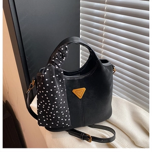 Détail du sac seau en cuir mat noir avec logo en métal et foulard à pois élégant
