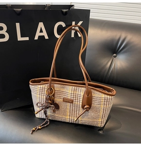 Detail der Vintage-Karo-Handtasche mit braunem Lederbesatz und Knotenaanhänger auf Sofa