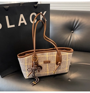 Detail einer Tweed-Handtasche mit Karomuster Ledergriff und Quastenanhänger auf Sofa