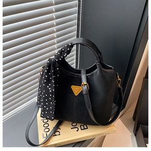 Détail du sac à main noir mat avec logo triangle jaune et écharpe à pois sur la poignée