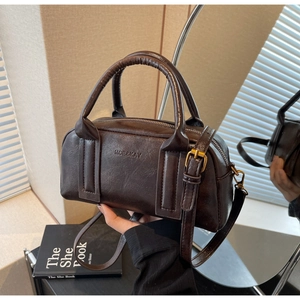 Detail of dark brown leather texture and embossed MOE&KAY brand logo on Boston bag