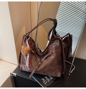 Detail of dark brown tote bag with plush bear charm and woven rope accessory in soft light