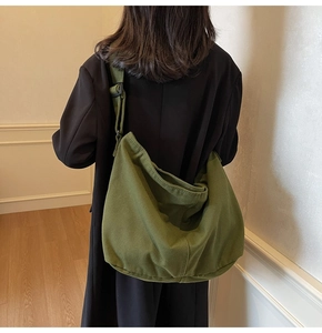 Model trägt eine große armee-grüne Canvas-Tasche über einem schwarzen Mantel