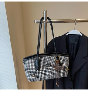 Detail der Hahnentritt-Tasche mit Lederriemen und einer metallischen Markenplakette