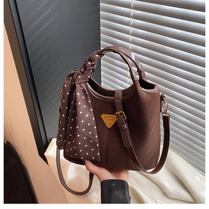 Détail du sac seau marron foncé avec logo doré, foulard à pois et bandoulière