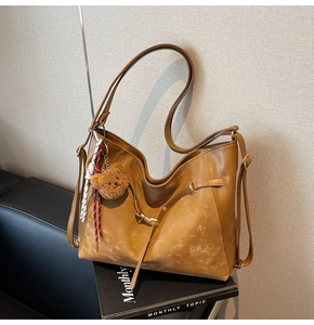 Detail of a brown leather tote bag featuring a teddy bear charm and textured finish