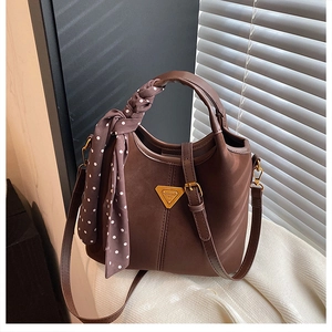 Gros plan d'un sac seau en cuir mat marron avec foulard en soie sur tricot blanc