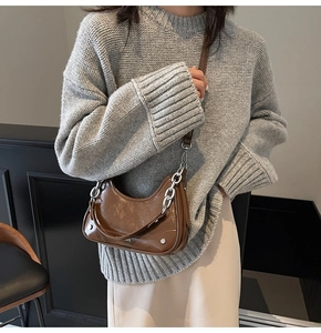 Détail d'un sac selle en cuir brillant marron avec bandoulière en chaîne métallique argentée