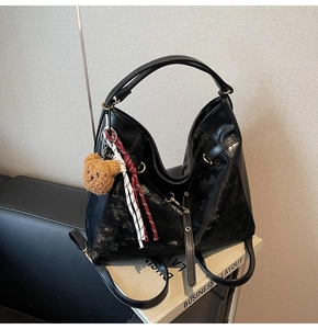 Detail of black large shoulder bag with plush bear charm and woven tassel decoration