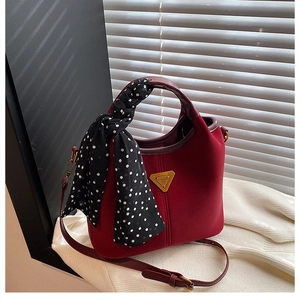 Détail du sac à main bordeaux en cuir mat avec foulard à pois et logo en métal doré