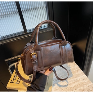 Detailed view of deep brown Boston bag with MCE&KAY logo on minimalist book backdrop