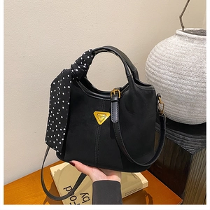 Détail du sac seau en cuir noir avec foulard à pois et logo triangle doré