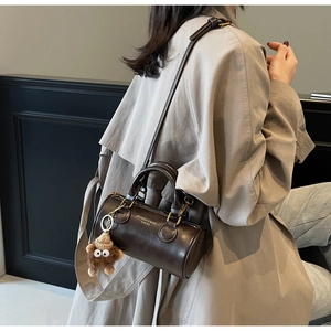 Detail of cylinder bag with plush charm on beige coat highlighting sleek leather