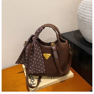 Détail du sac seau marron avec foulard à pois et logo triangulaire doré élégant