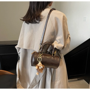 Detail of a dark brown cylinder bag with polished leather finish and cute plush charm