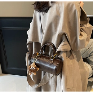 Detail of dark brown cylindrical Boston bag with leather handles and monster charm