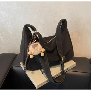 Detail of a black nylon tote bag with a cute plush pendant on a leather sofa surface