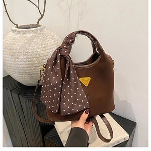Détail du sac à main en cuir mat marron foncé avec foulard à pois et logo triangle