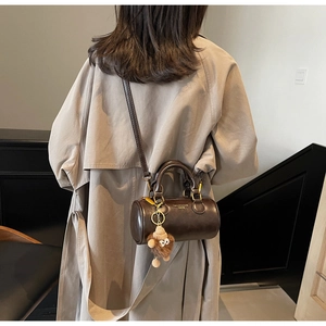 Detail of a brown cylindrical leather crossbody bag with a plush lion keychain