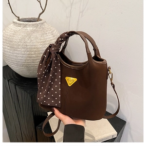 Gros plan du sac seau marron mat vintage avec foulard à pois et plaque métallique décor