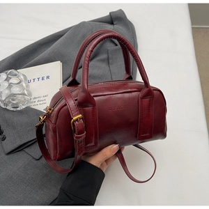 Macro shot of the burgundy leather texture and vintage gold hardware on a Boston bag