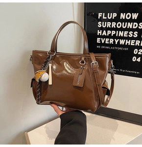 Detail of dark brown leather tote bag showing a side pocket and decorative baseball charm
