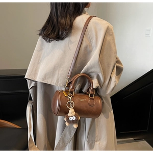 Close-up of a brown vintage cylinder bag with gold lettering and a plush charm detail