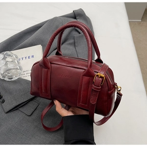 Close-up of wine red Boston bag with textured leather, brand logo and hardware details