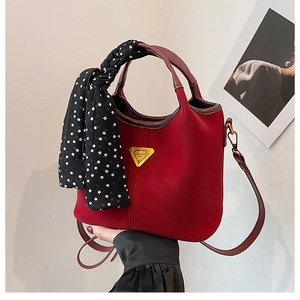 Détail du sac seau rouge mat avec un foulard à pois noir et blanc sur l'anse