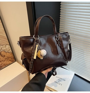 Detail of dark brown leather tote bag featuring baseball charms and side pocket
